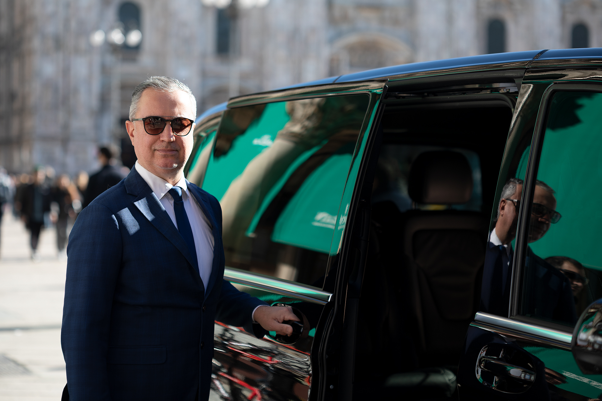 Professional chauffeur opening the door of a Mercedes V-Class for a business client in Milan