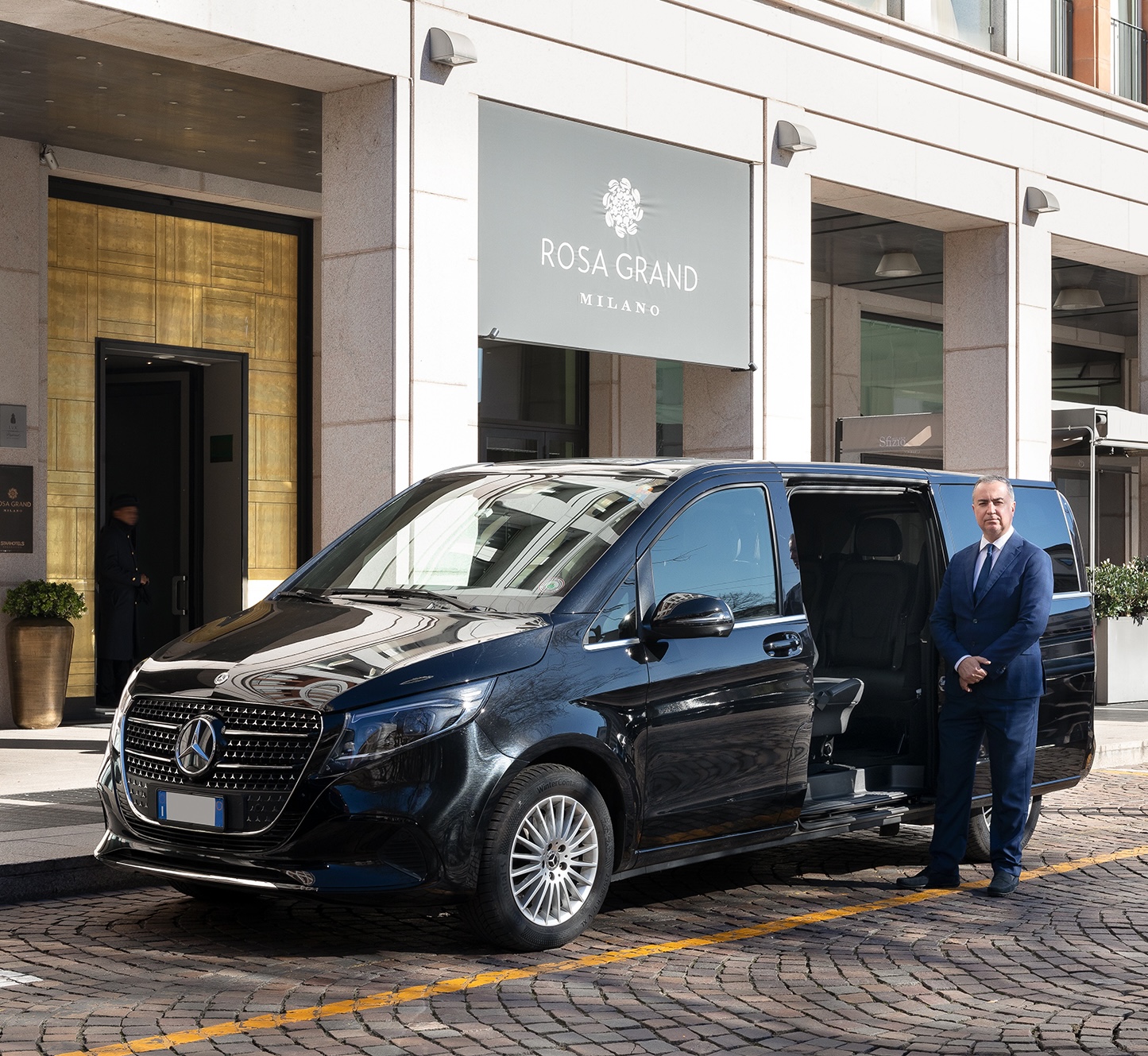 Professional chauffeur standing next to Mercedes V-Class outside a luxury hotel in Milan